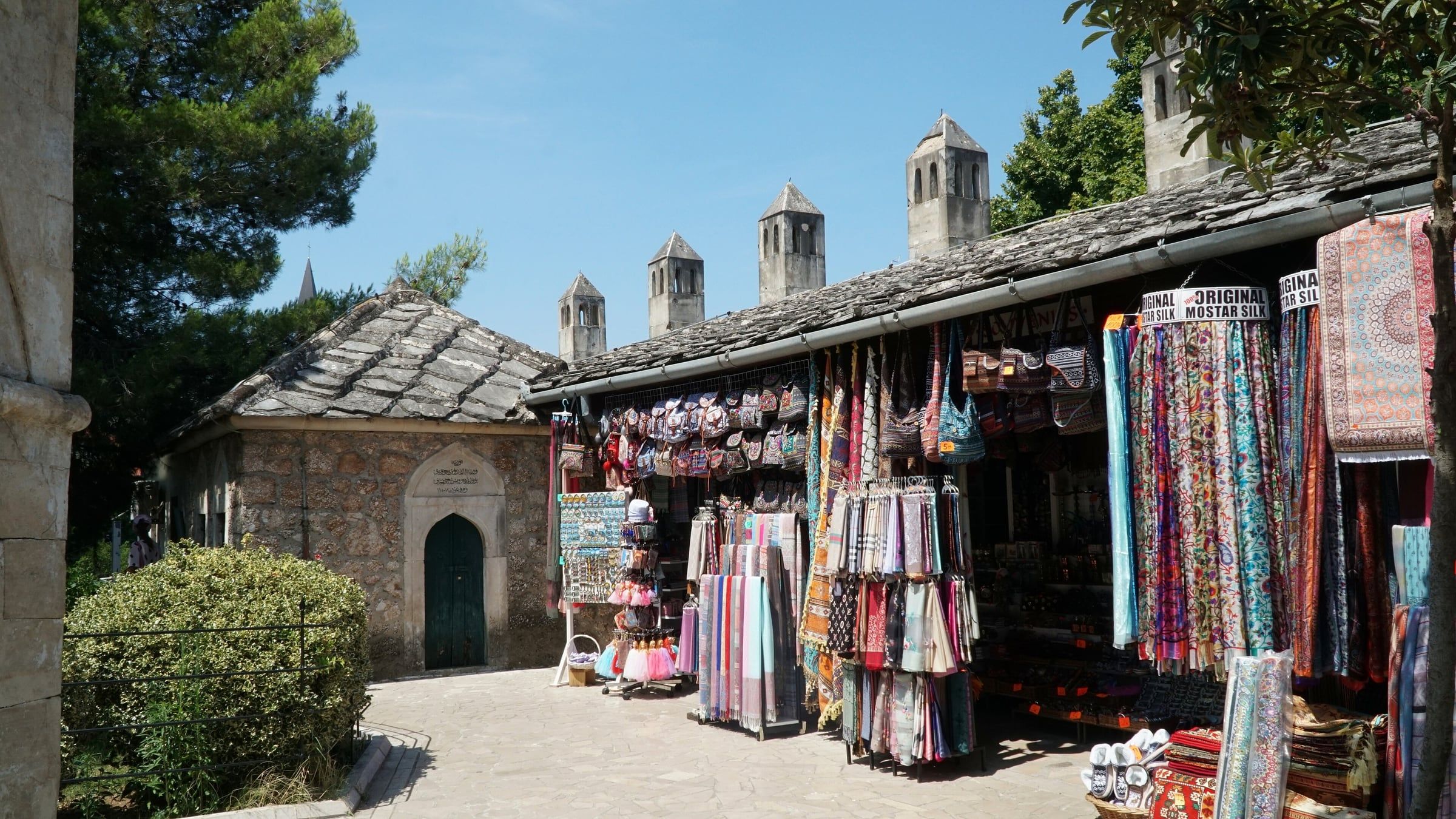 Stone-roofed buildings and stalls hung with rugs and scarves in the courtyard of the Koski Mehmed Pasha Mosque.