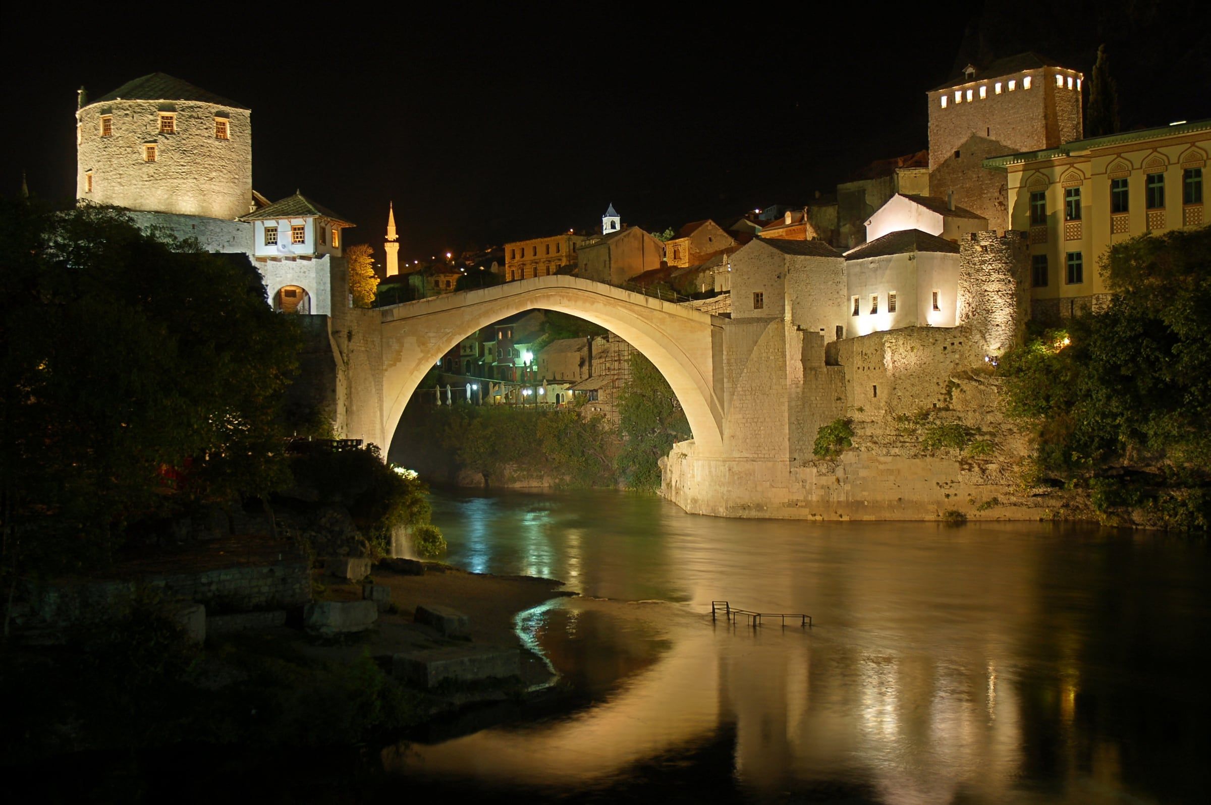 The Old Bridge lit up at night, its arch and towers reflected in the dark river below.